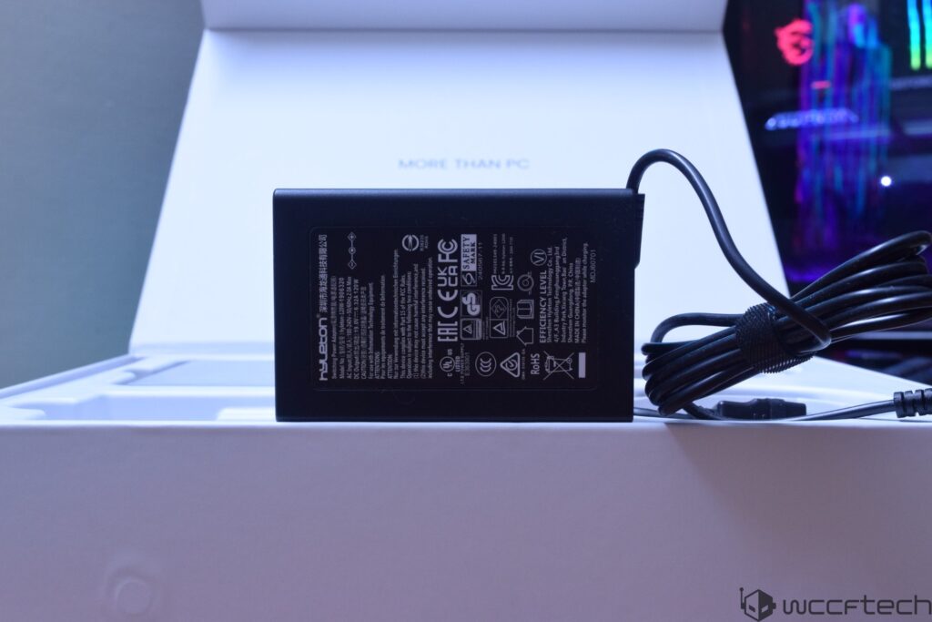 A Hyuboton power adapter is displayed with certification logos and specifications visible against a blurred background featur