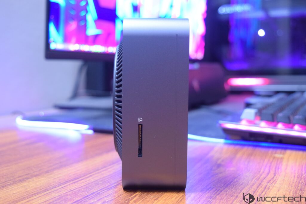 A mini PC is placed on a desk with a monitor displaying vibrant colors and a keyboard in the background.