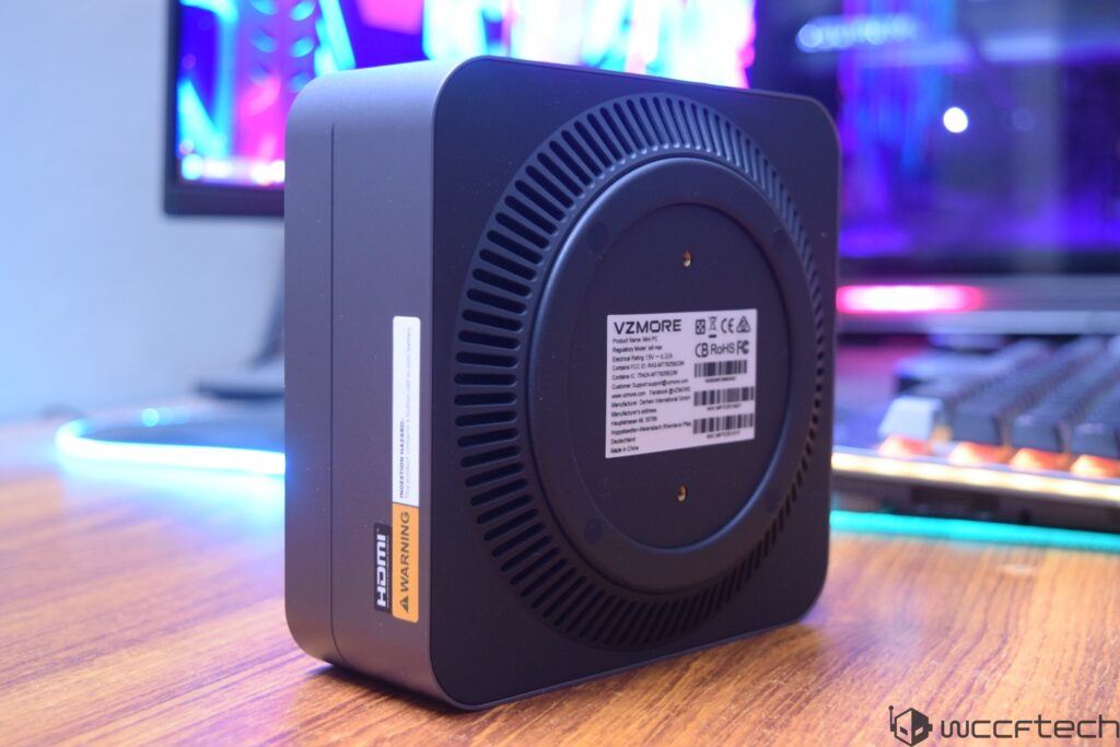 A VZMORE mini PC with a prominent 'HDMI WARNING' label is placed on a wooden desk next to a mechanical keyboard and a monitor