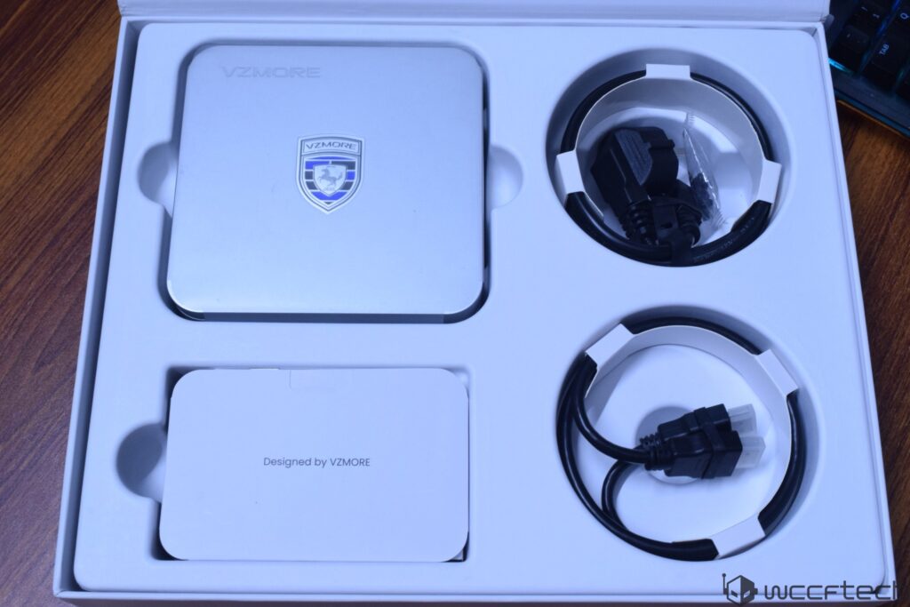 A VZMORE package containing a metal device with the VZMORE logo and two cables, alongside a card labeled 'Designed by VZMORE'
